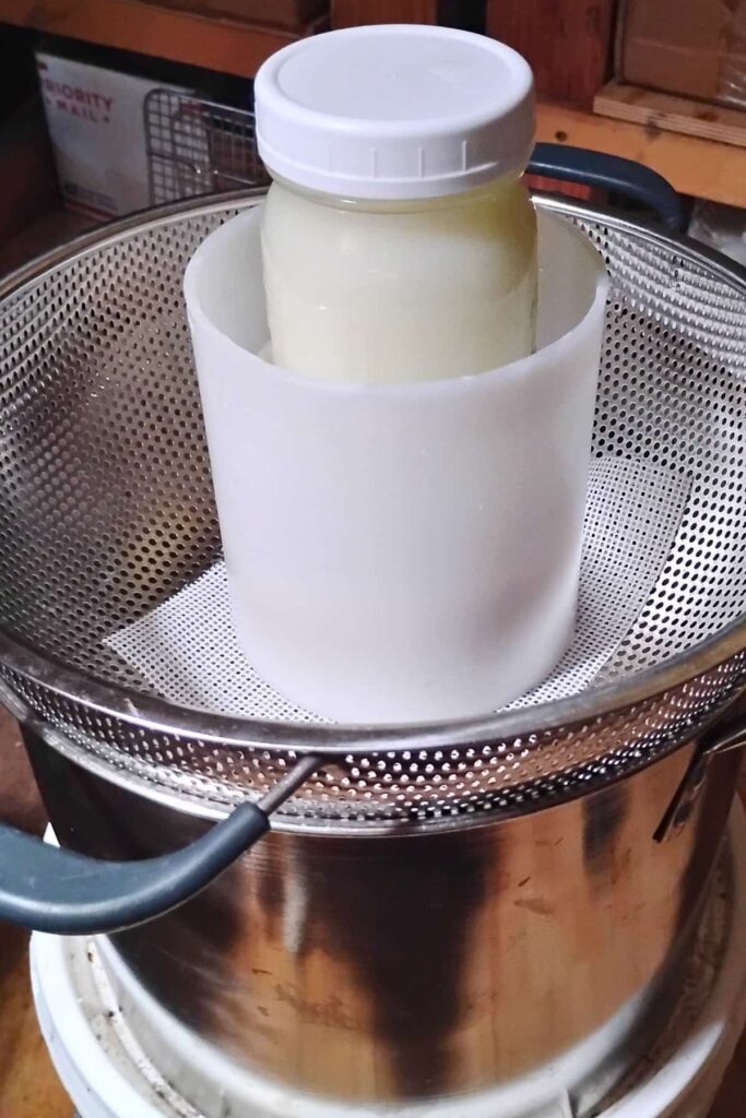 a mason jar filled with warm whey in a colander over a pot.