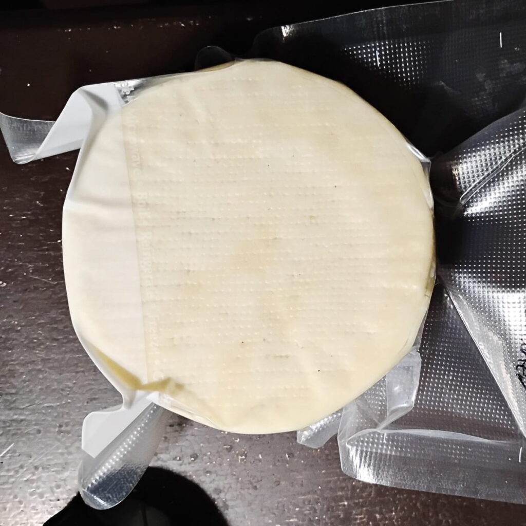 a loaf of bel paese cheese vacuum sealed in a foodsaver bag for aging in the fridge.