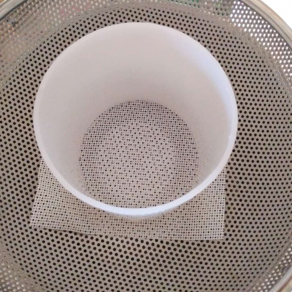 colander with a draining mat and an empty cheese form in it.