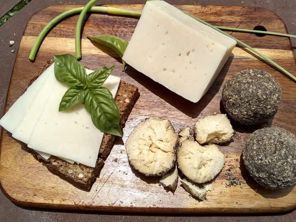 photo of a spread of cheese on a wooden cutting board. a chunk of bel paese cheese, several belper knolls and a slice of seeded rye bread with slices of bel paese cheese on top.