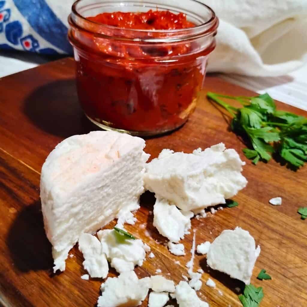 photo of a chunk of soft feta cheese and some smaller chunks around it. behind it is a jar filled with ajvar pepper spread.