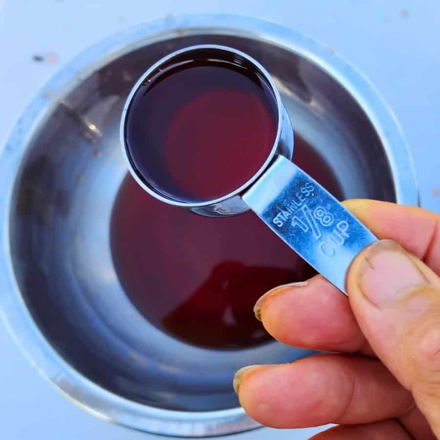 a bowl filled with mimosa flower syrup and a hand holding a one ounce measure with syrup to use in making soda