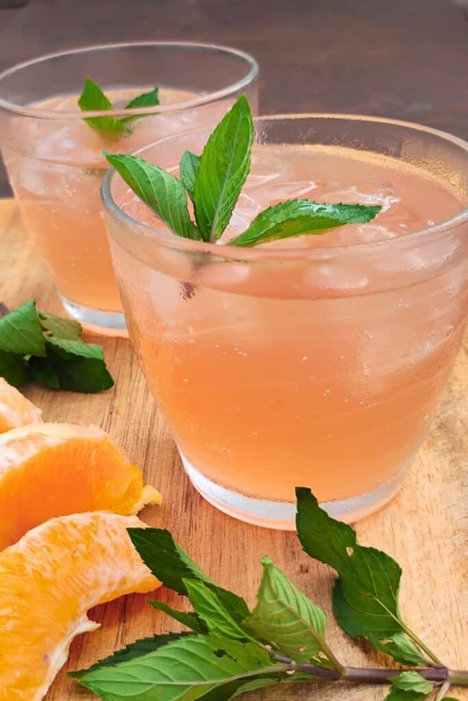 photo shows two glasses filled with mimosa flower soda on ice and decorated with mint sprigs and oranges.