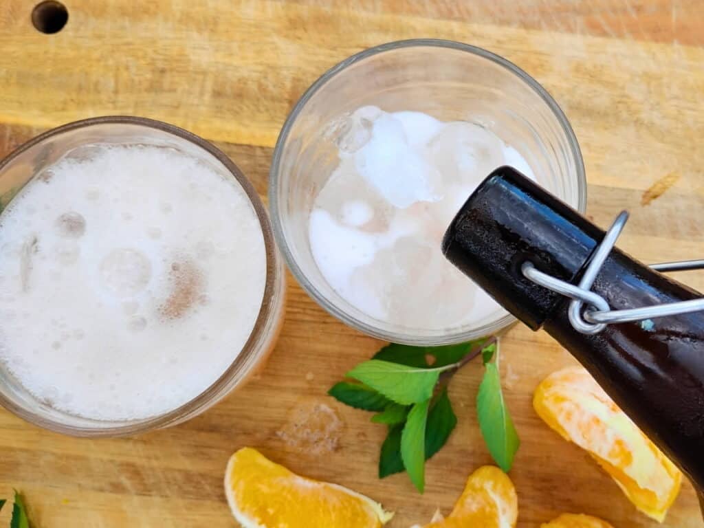 photo shows two serving glasses getting filled with fizzy mimosa flower soda from a bottle.